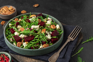 Arugula, beet and blue cheese salad with pecan nuts in a plate with fork on black table background. healthy vegetarian food