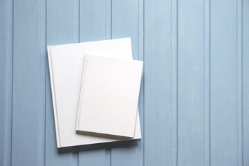 Two paper books with white covers without drawings on a wooden surface.