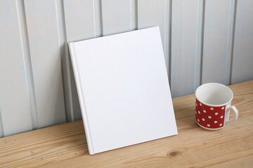 Mockup a paper book, an album with an empty cover and a mug on a wooden table, the creator of the...