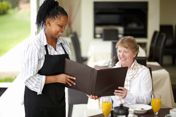 Waitress, service and senior woman in a restaurant for breakfast or lunch at a hotel with a menu and choice of food. Friendly, order and elderly person happy on vacation or holiday for hospitality