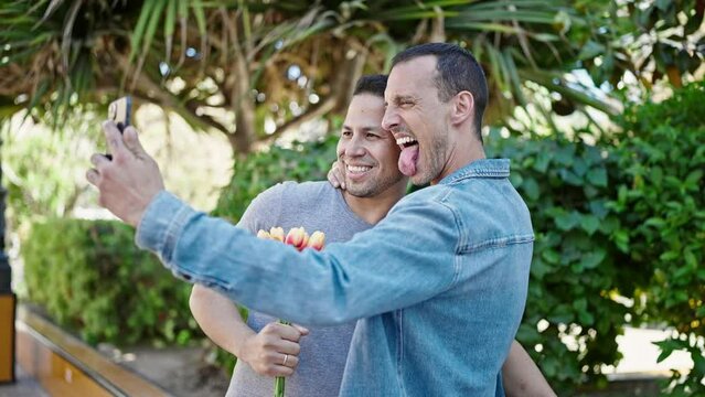 Two men couple make selfie by smartphone holding bouquet of flowers at park