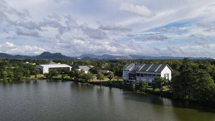 A breathtaking view of a lake with a large building situated at its edge. The green grass and trees around the lake add to the scenic beauty, while the sky is filled with beautiful clouds.