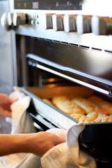 Hands, closeup and tray from oven for bread, baking product or food for small business, cafe or restaurant. Chef, baker or person with cloth for safety in bakery, coffee shop or food industry startup
