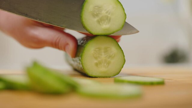 Woman cutting fresh cucumber. Female hands of cook slicing cucumber with knife on wooden board. Cooking healthy food from vegetables.