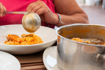 Lady pouring a saucepan from the pot to the plate of rice with seafood in a Portuguese restaurant, Close-up.