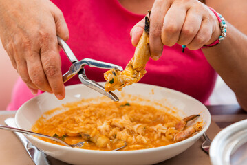Woman's hands with tongs breaking a lobster leg on a plate of rice with seafood. Close-up.