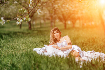 woman garden. she sleeps on a white bed in the fresh spring grass in the garden. Dressed in a blue nightgown.