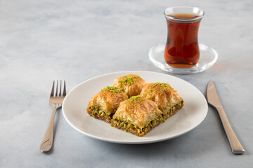 Pistachio baklava on a white plate with Turkish tea.A plate of traditional baklava on light blue background
