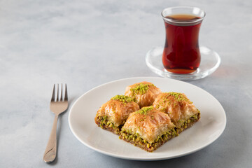 Pistachio baklava on a white plate with Turkish tea.A plate of traditional baklava on light blue background 