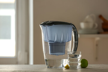 Water filter jug with glass and lime on table in kitchen