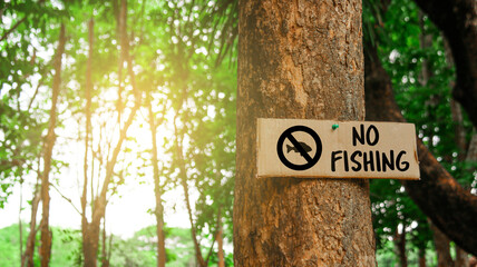 Brown paper label with drawing of fish in no sign with the text no fishing on tree trunk with...