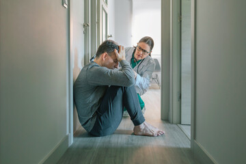 Female psychiatrist reassuring and helping with empathy to male patient sitting on the room floor of mental health center