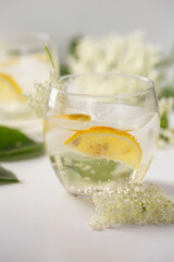 A delicious drink made of elderflowers and lemon with ice on a light background