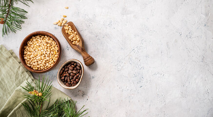 Pine nuts in a bowl and wooden scoop  on a napkin on a light texture background with branches of pine needles. The concept of a natural, organic and healthy superfood and snack.