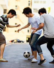 Friends in street playing football together for sports, fun and happy energy with urban games in...