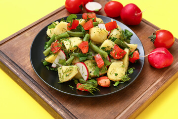 Plate of tasty Potato Salad with vegetables on yellow background