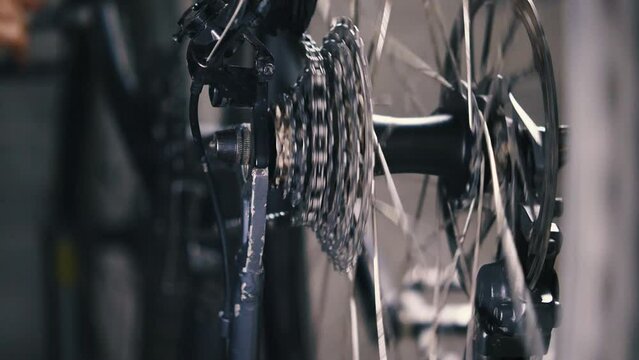 The bike's cassette and chain travel from small chainring to large chainring and back. The repairman's hand twists the pedals to check the rear derailleur. Close-up, slow motion