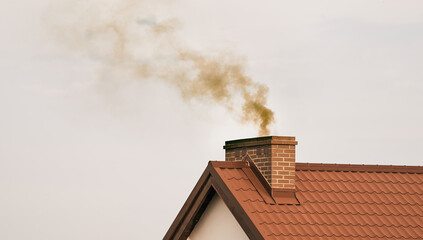 Dark smoke comes out of the chimney of a modern house in winter. Heating with solid fuel. The concept of environmental pollution - obrazy, fototapety, plakaty