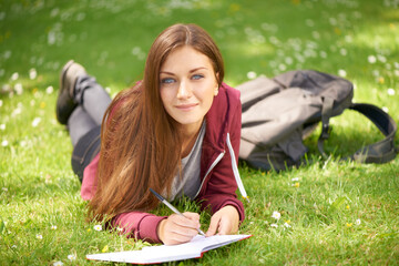 Woman, student and grass for writing, portrait or planning at university, campus or park for studying. Girl, book and pen for education, learning or brainstorming ideas on lawn at college in sunshine