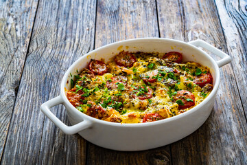 Bread casserole with mozzarella cheese, tomatoes and scrambled eggs on wooden table