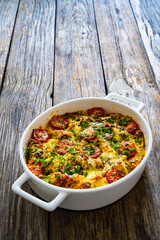 Bread casserole with mozzarella cheese, tomatoes and scrambled eggs on wooden table