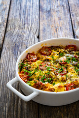 Bread casserole with mozzarella cheese, tomatoes and scrambled eggs on wooden table