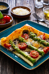 Baked puff pastry, green asparagus with mozzarella cheese, mushrooms and cherry tomatoes on wooden table
