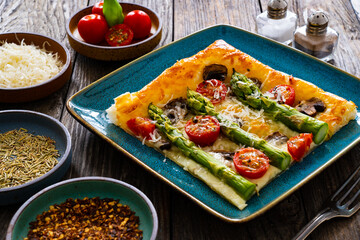 Baked puff pastry, green asparagus with mozzarella cheese, mushrooms and cherry tomatoes on wooden table
