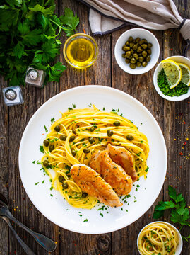 Chicken piccata with spaghetti and capers in sauce on wooden background
