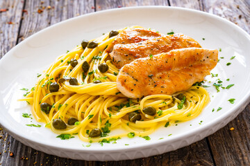 Chicken piccata with spaghetti and capers in sauce on wooden background

