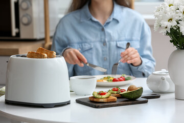 Woman having breakfast at table with modern toaster, delicious sandwiches and cup of coffee