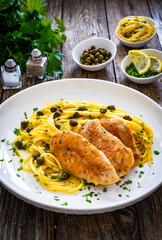 Chicken piccata with spaghetti and capers in sauce on wooden background

