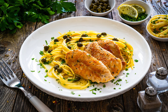 Chicken piccata with spaghetti and capers in sauce on wooden background
