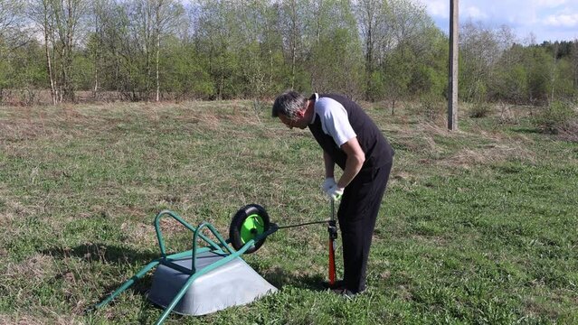 Using hand operated pneumatic pump, farmer inflates pneumatic tire of one wheeled garden cart.