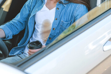 A faceless girl spilling coffee or tea on herself while driving a car. Spoiled clothes. Concept of...