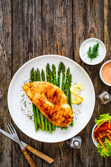 Grilled chicken breast and green asparagus on wooden table