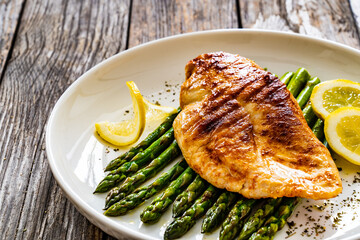Grilled chicken breast and green asparagus on wooden table