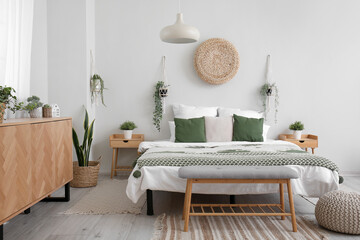 Interior of light bedroom with cozy bed, wooden cabinet and hanging houseplants