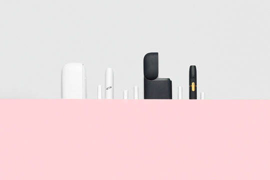 Modern electronic cigarette devices and accessories for vaping, heat-not-burn technology, and tobacco alternatives on pink and white background