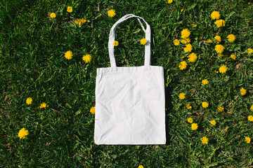 White cotton or mesh bag on dandelion green grass background. Zero waste, no plastic eco friendly shopping, recycling concept. Blank mockup shopper with place for artwork or text. Flat lay, copy space