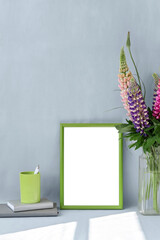 Empty fresh green picture frame, flowers lupine bouquet in vase, stationery on light blue background with sunlight abstract pattern