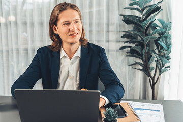 Businessman in black suit working on laptop at his workspace desk. Smart executive researching financial data and planning marketing strategy on corporate laptop at modern workplace. Entity
