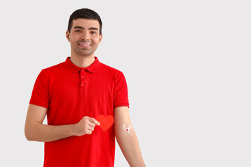 Young blood donor with applied medical patches and paper heart on light background