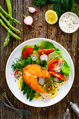 Seared salmon steak with fried green asparagus and fresh vegetable salad served on wooden table
