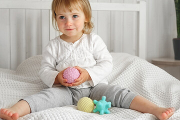 Cute baby girl playing tactile knobby balls. Young child hand plays sensory massage ball. Enhance...
