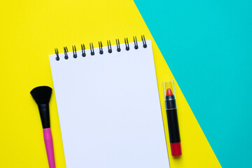 Set of cosmetics brushes and note book on yellow and green table background