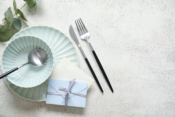Clean plate with blank invitation card, cutlery and eucalyptus branch on white table