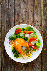 Seared salmon steak with fried green asparagus and fresh vegetable salad served on wooden table
