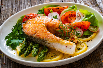 Seared salmon steak with fried green asparagus and fresh vegetable salad served on wooden table
