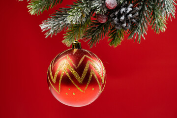 Shiny ball on a snow-covered branch of a Christmas tree on a red background, place for your text